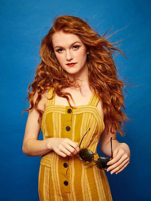 Redheaded fashion model in yellow jumper with blue studio background photographed by clothing apparel photographer Kate Benson.