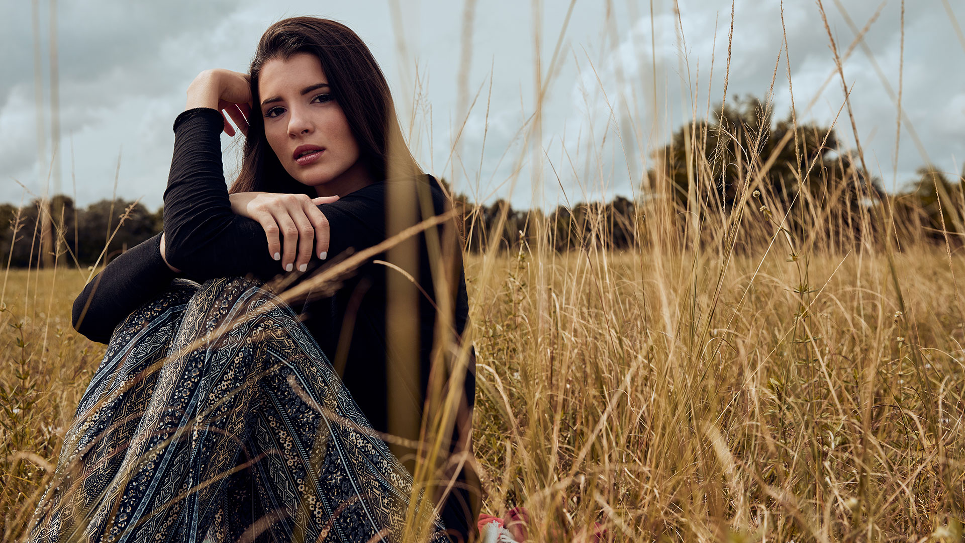 Fashion model sitting in field of tall grass photographed by women's apparel clothing photographer Kate Benson.
